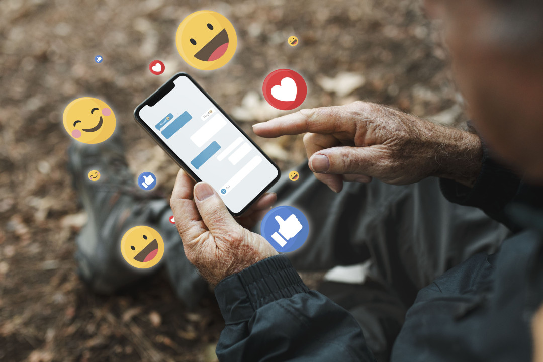 Person using smartphone with Facebook emojis floating around.